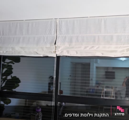 וילון רומי לבן תלוי על חלון גדול